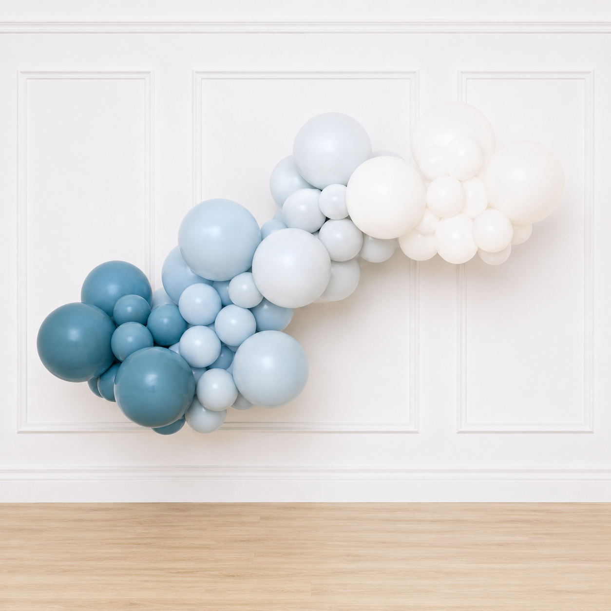 Blue and white organic balloon garland displayed on a white wainscoting wall with white oak flooring for baby showers, birthdays, and event backdrops.